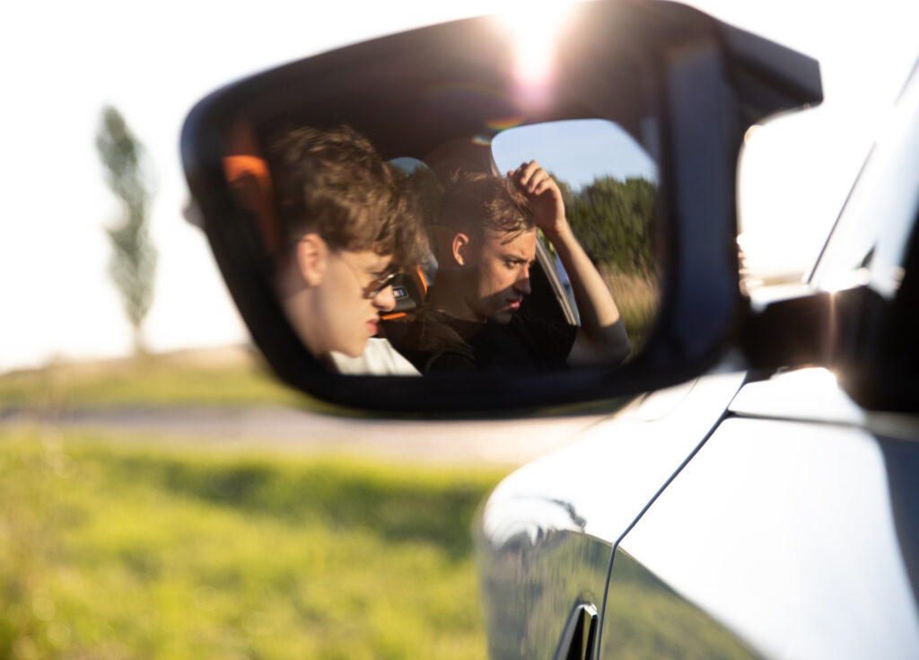 Two young men can be seen in a car mirror